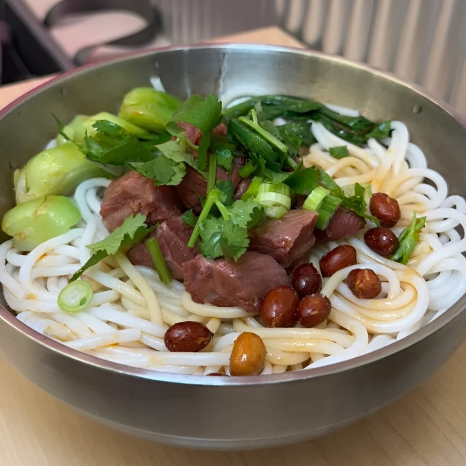 Loong Noodles' beef noodle dish with bok choy, peanuts, and cilantro in a metal bowl.