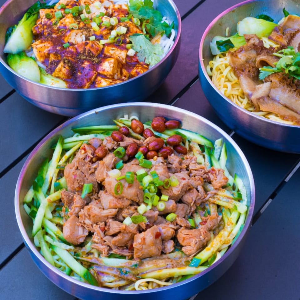 Three bowls of Loong Noodles, including spicy tofu, duck, and pork with peanuts and cucumber.